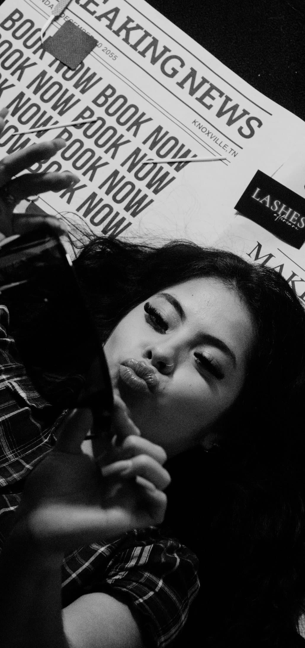 Black and white photo of Maria lying on Breaking News newspapers, blowing a kiss