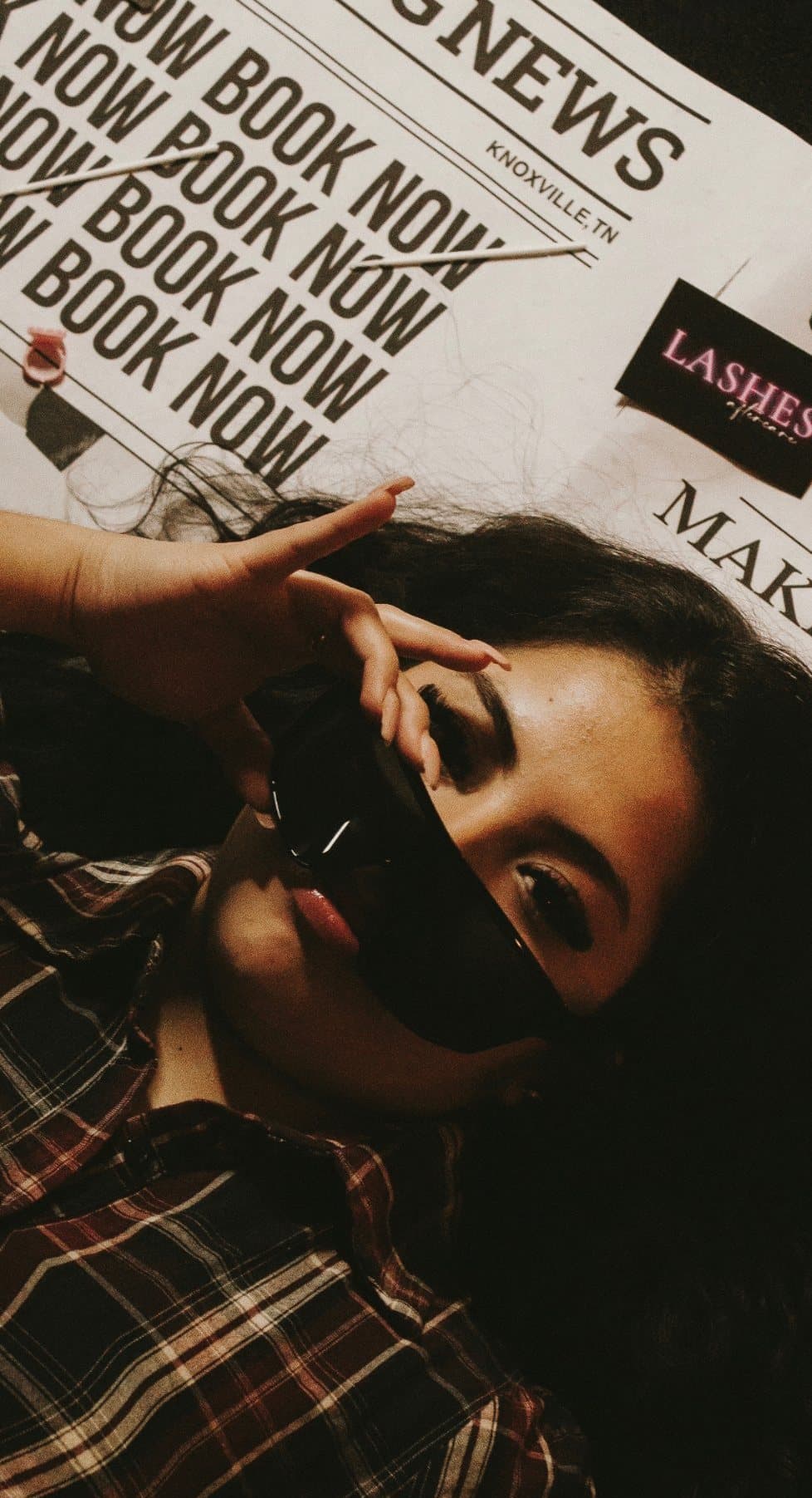Maria lying on a spread of Book Now newspapers, holding sunglasses over one eye