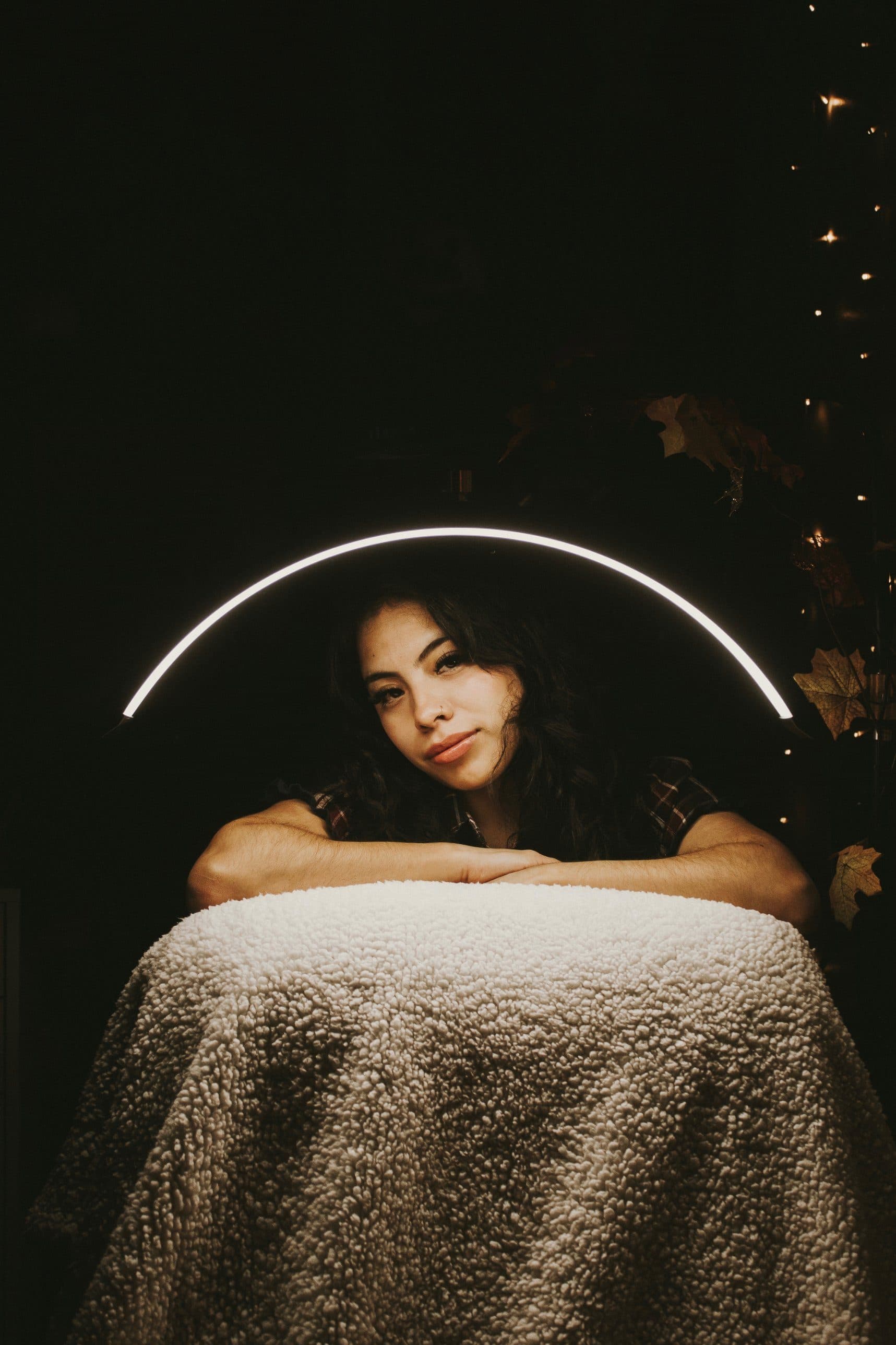 Maria resting her arms on a lash bed under a glowing arch light in her dark studio