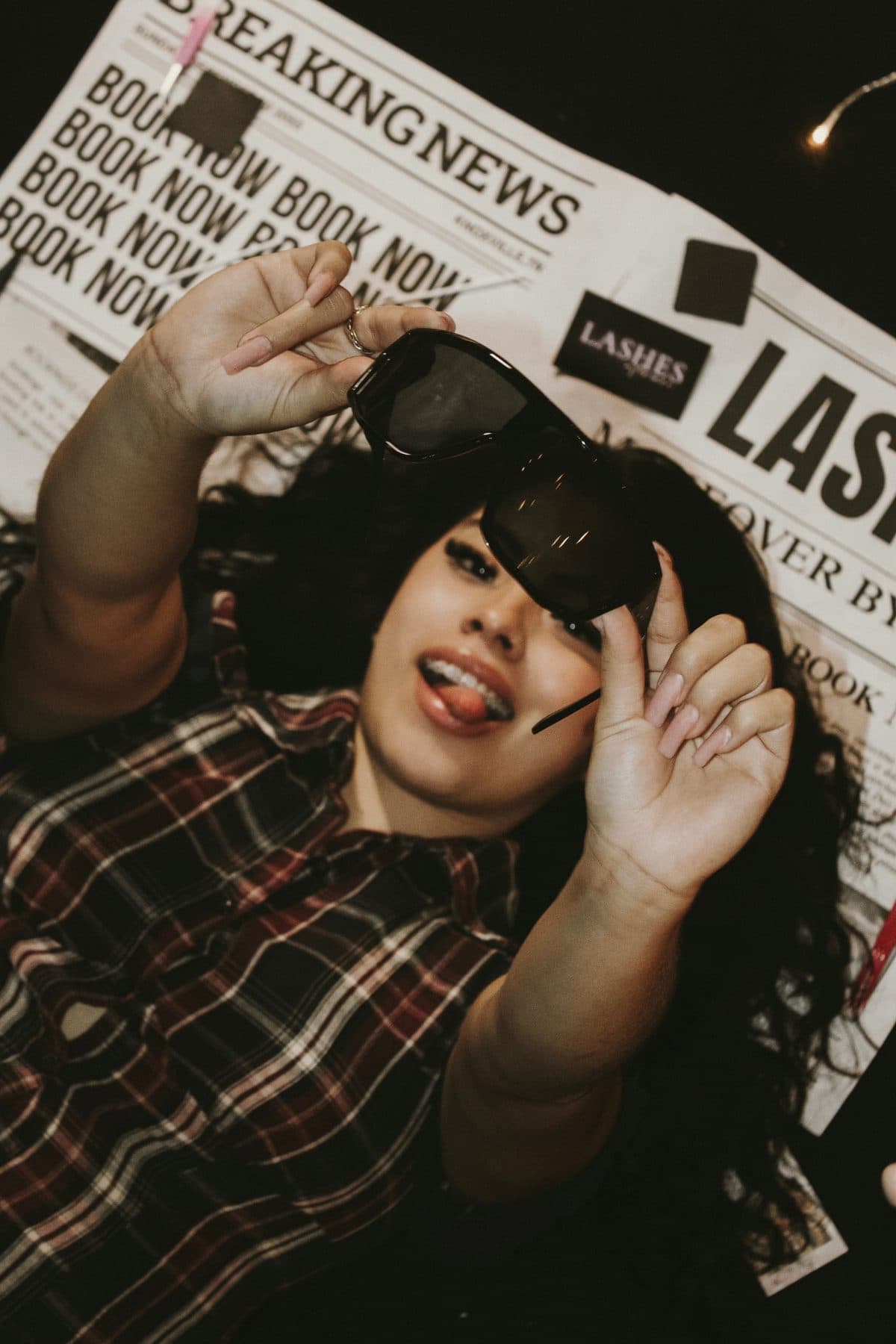 Maria laughing on a spread of Makeover by Maria newspapers, lifting a pair of sunglasses