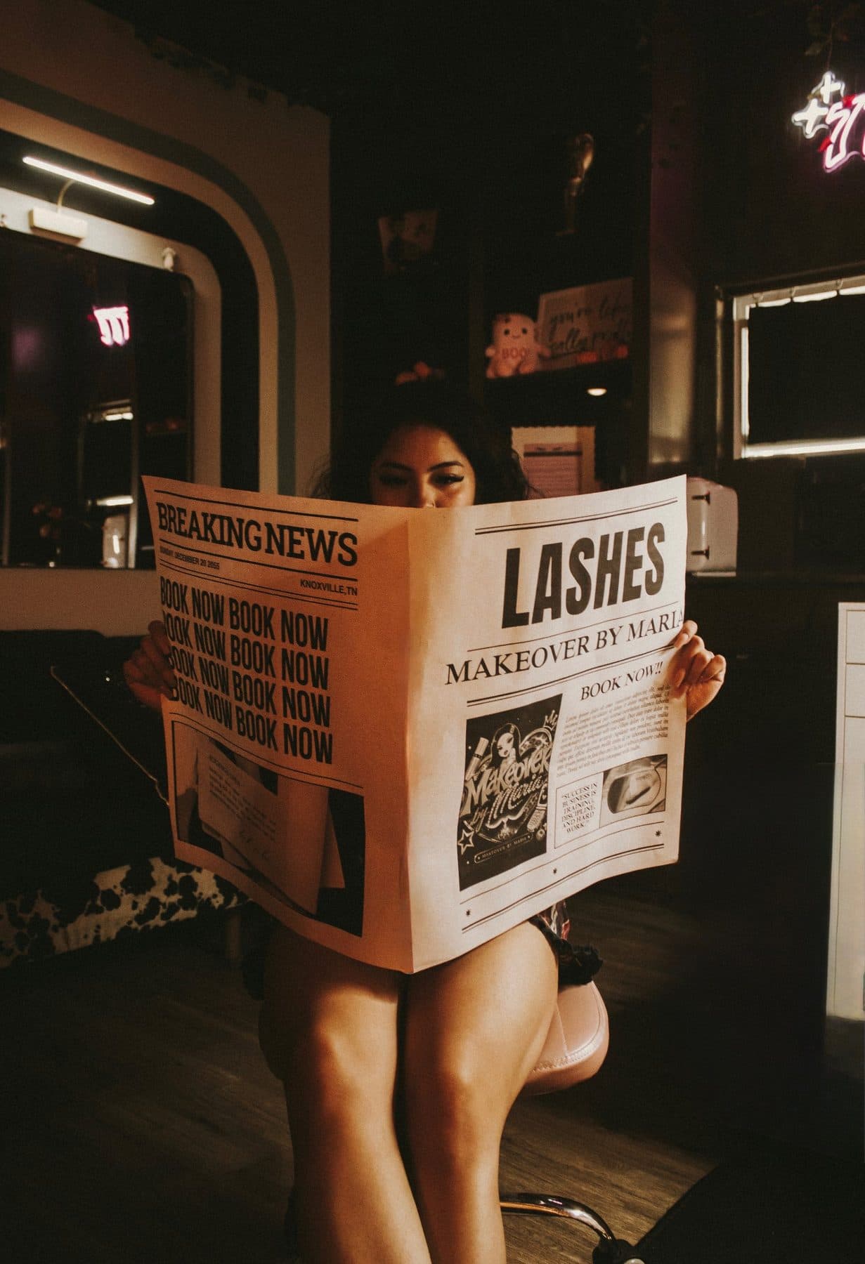 Maria in her salon reading a newspaper with the headline Lashes, Makeover by Maria