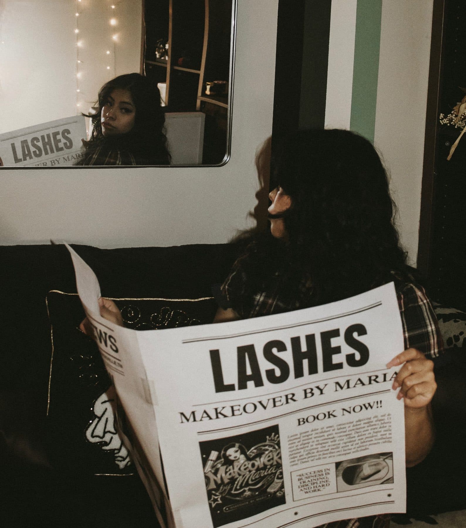 Maria in her studio holding a Lashes newspaper, her reflection looking back from the mirror