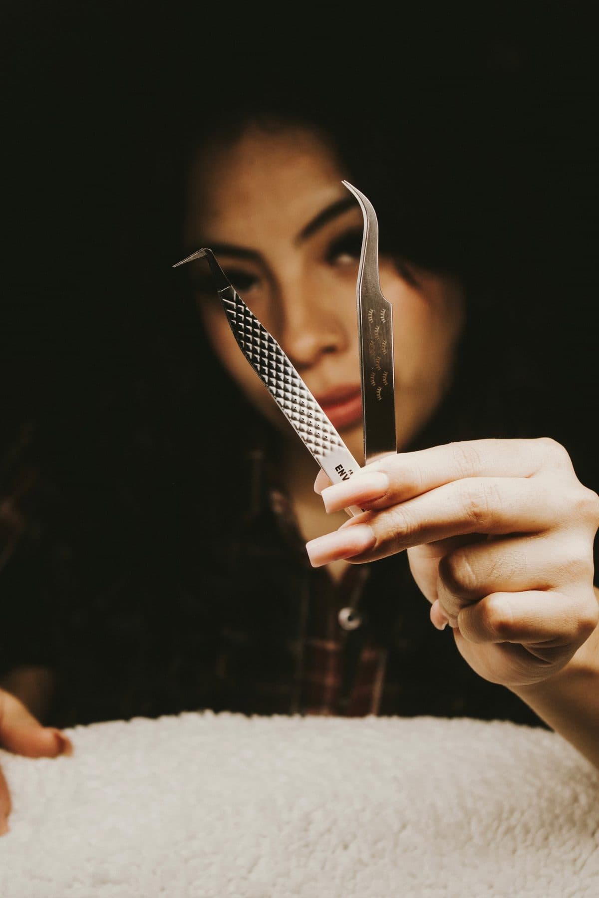 Maria holding lash tweezers up beside her eye, wearing her own lash extensions